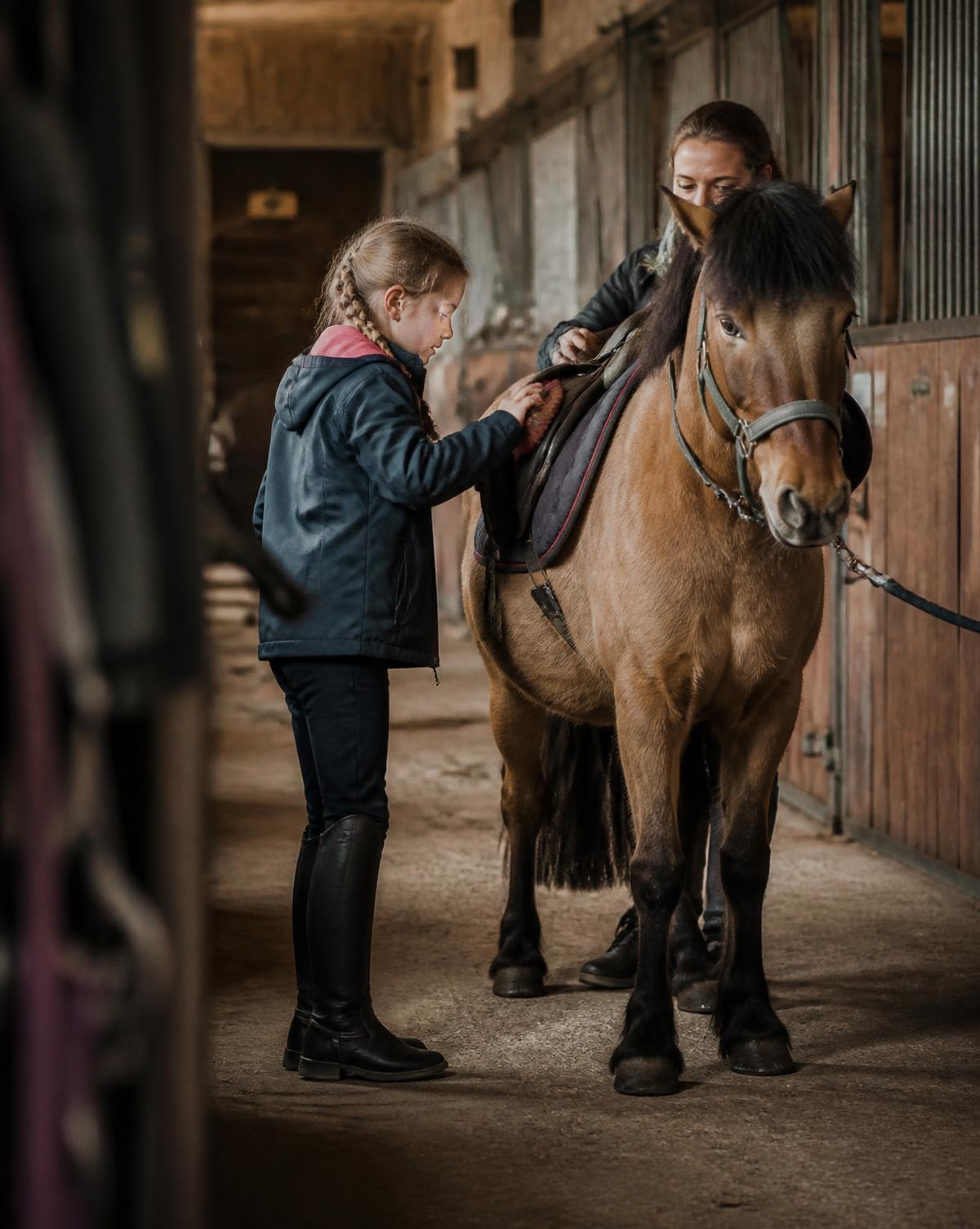 Kind poetst een pony in de stalgang, geholpen door een volwassene